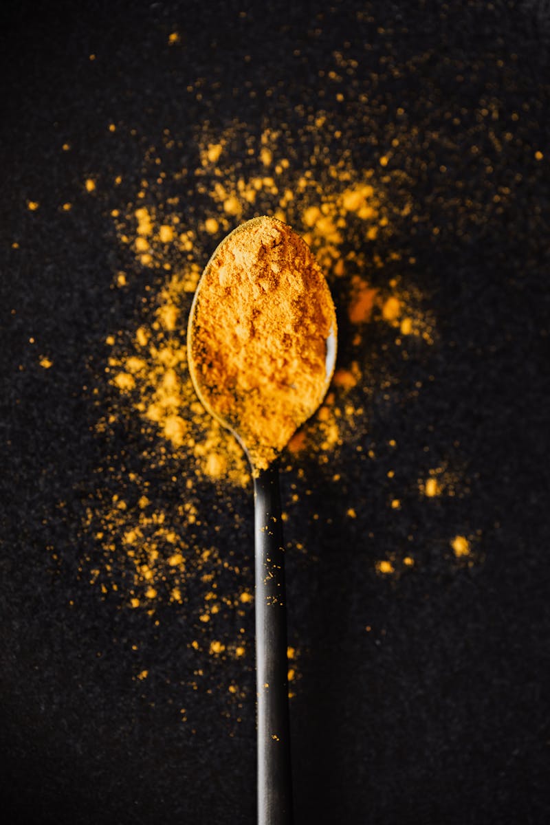 Unveiling the Wonders of Curcuma Longa: A Natural Marvel for Health and Wellness 2 From above of creative composition of bright ground turmeric on metal tablespoon spilled on black table